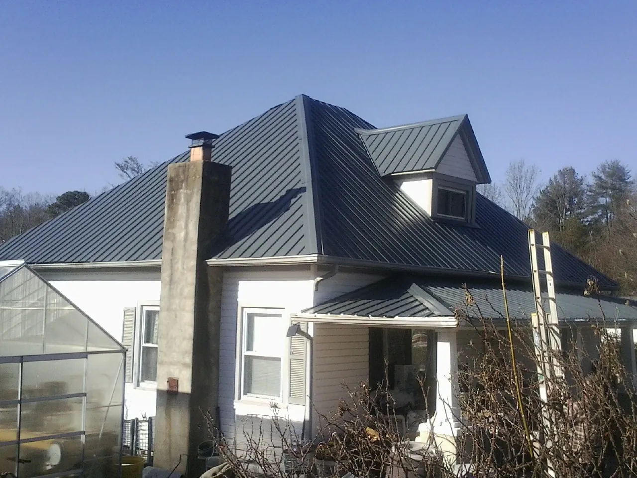 Dark blue standing seam metal roof on a white farmhouse with dormer — Slate & Tile Roof Repair by Roofing Brothers in Alamo